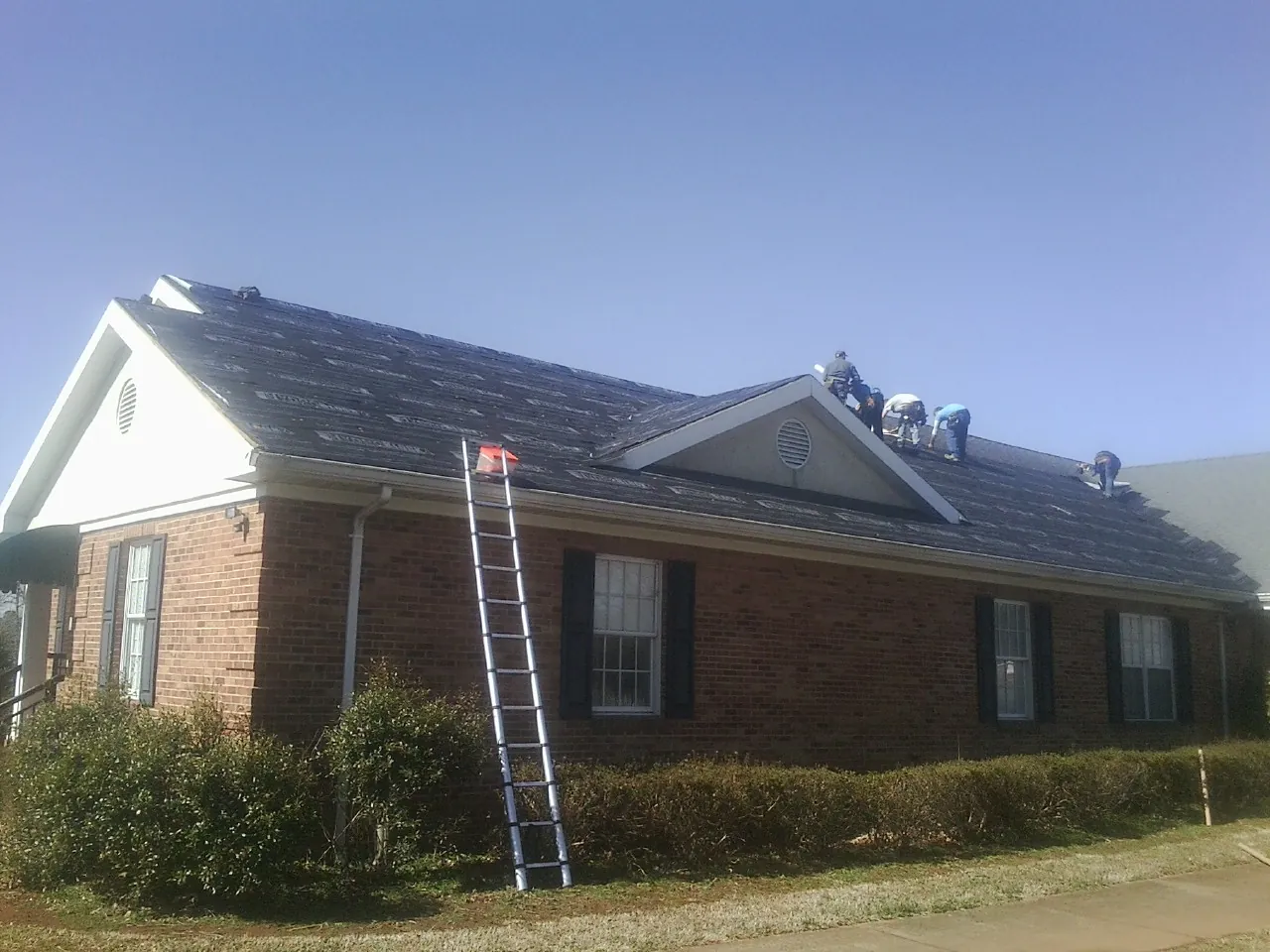 Crew tearing shingles off a brick ranch roof with a ladder set — Emergency Roof Repair work by our crew in Kendall