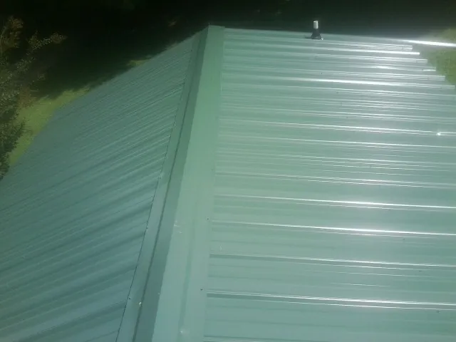 New green metal panels meeting at the ridge of a roof — Flat Roof Repair work by our crew in Kendall