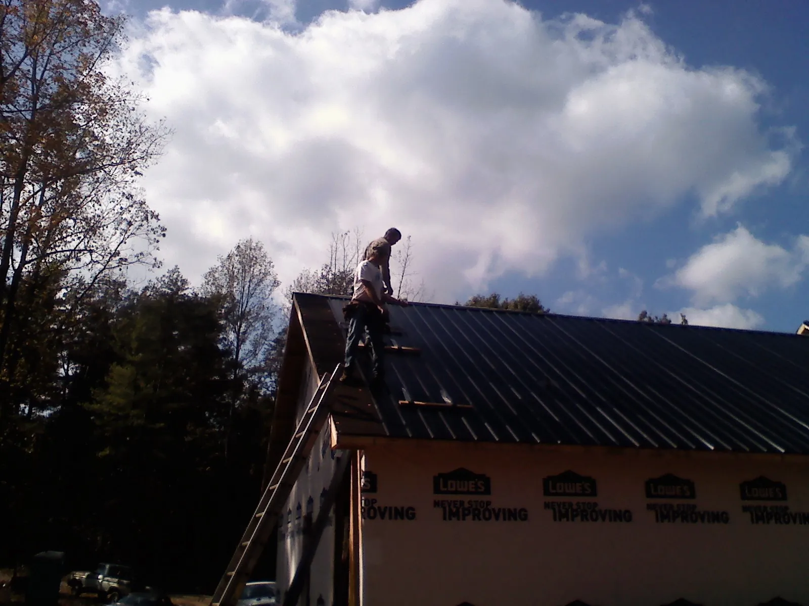 Roofer fastening dark metal panels high against a cloudy sky, from a Roof Inspection job in Kendall